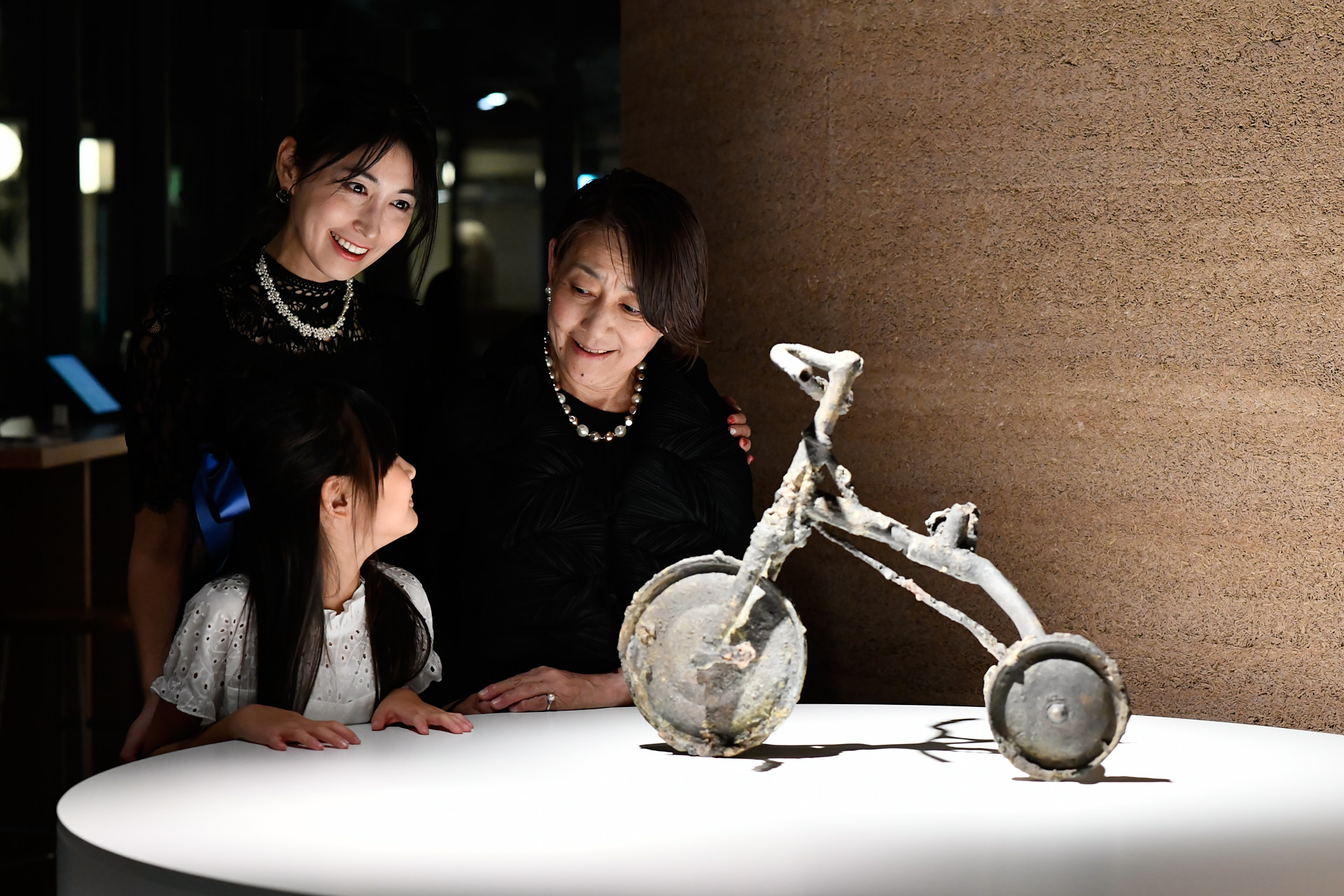 Photo de la famille Tetsutani, 3 femmes de générations différentes, contemplant le tricycle - format paysage - ©Zoé Aubry